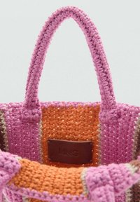 Sac fourre-tout en tissu tressé présentant de la laine rose et orange avec une finition texturée. Étiquette en cuir marron avec "MNG" accentue l'intérieur.
