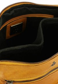 Interno di una borsa in pelle marrone con rivestimento in tessuto nero, dotata di chiusura con zip e un piccolo dettaglio in pelle con un logo metallico.