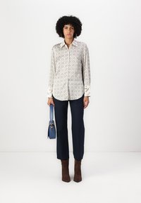 Long-sleeve shirt with a white and beige geometric pattern, paired with navy trousers and brown ankle boots. Blue handbag with a strap.