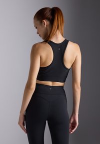 Black ribbed sports bra with a racerback design, paired with high-waisted black leggings, featuring subtle stitching details and logo accents.