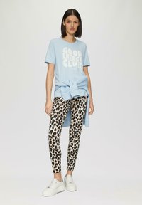 Lichtblauw t-shirt met de tekst "GOOD ENERGY CLUB", gecombineerd met beige legging met luipaardprint en witte chunky sneakers. Gemaakt van een katoenmix.