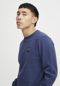 Navy blue sweatshirt made of cotton, featuring a crew neckline, long sleeves, and a circular embroidered logo on the chest.