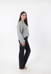 Grijze cropped sweater met lange mouwen, gecombineerd met zwarte jeans en sandaaltjes met bandjes. Eenvoudige textuur en een relaxte pasvorm.