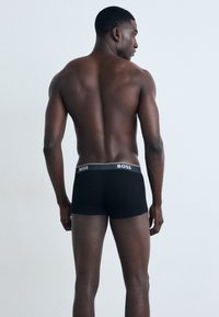Schwarze Boxershorts mit einem weißen "BOSS"-Logo auf dem elastischen Bund, mit einer engen Passform und weichem Stoff, von hinten präsentiert.