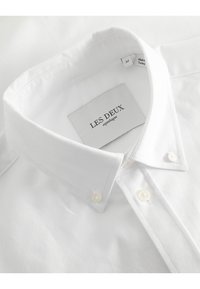 Camicia bianca button-up in cotone testurizzato, con colletto classico, bottoni perlati bianchi e un'etichetta con il marchio "LES DEUX".
