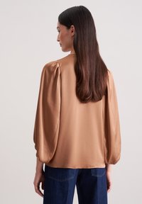 Kortærmet, kobberfarvet Bluse med en glat tekstur, puffede ærmer og rund halsudskæring, parret med mørkeblå jeans.