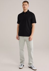 Črna rebrasta polo majica s ovratnikom, v kombinaciji z svetlo sivo hlačami in črnimi ter belimi supergami. Minimalističen dizajn in kratki rokavi.