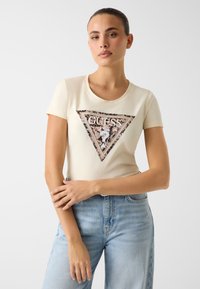 Kremowy T-shirt z krótkim rękawem z trójkątnym nadrukiem logo o mieszanym wzorze, zdobionym cekinami, z eleganckim okrągłym dekoltem.