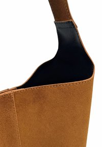 Sac en cuir suédé marron avec un intérieur en cuir noir ; il présente une sangle robuste et une surface lisse et texturée. Design minimaliste avec des accents cousus.