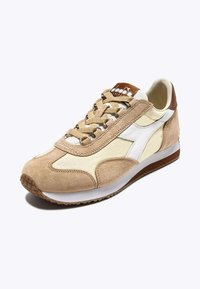 Sneaker beige in suede con pannelli in stoffa crema, accenti marroni, lacci testurizzati e una suola intermedia bianca. Presenta punta rotonda e suola in gomma con motivo.