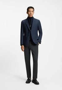 Navy blazer with textured fabric, two front pockets, paired with dark gray pants and black loafers. Standalone on a white background.