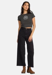 Dark gray cropped t-shirt with white graphic, high-waisted black wide-leg jeans, and brown ankle boots with elastic sides.