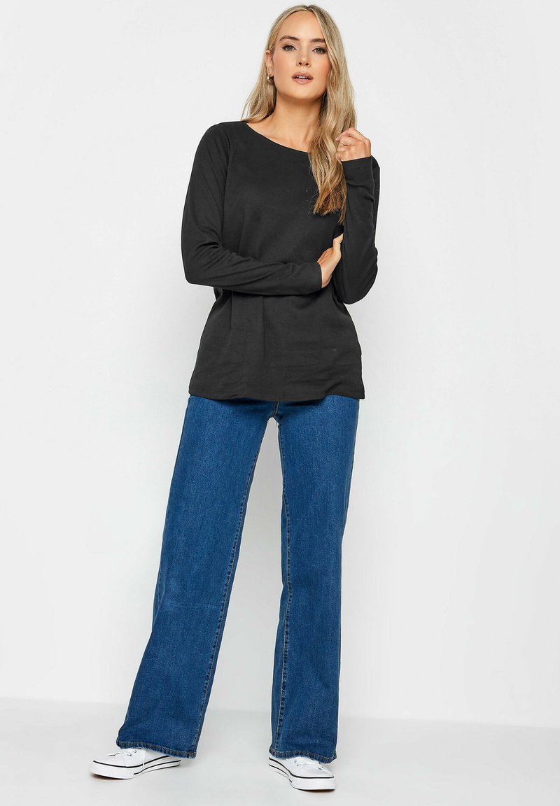 Schwarzes Langarmoberteil mit runder Halslinie, kombiniert mit lockeren blauen Jeans und weißen Sneakers. Einfaches Design, keine sichtbaren Muster.