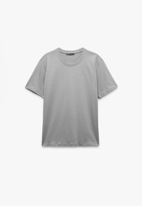 Camiseta gris claro con cuello redondo, mangas cortas y una textura suave. El diseño es simple, sin patrones ni acentos.