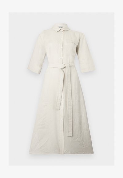 Μπεζ μακρύ πουκάμισο-φόρεμα με μανίκια τρία τέταρτα, κουμπιά στο μπροστινό μέρος, τσέπη στο στήθος, γιακά και ζώνη από το ίδιο ύφασμα δεμένη στη μέση.