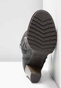 Bottine noire à tige texturée, fermeture éclair latérale et talon superposé. La semelle présente un motif de bande de roulement en zigzag pour une meilleure adhérence.