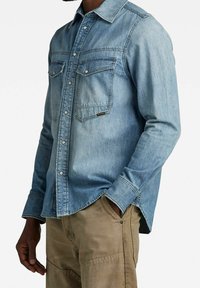 Lichtblauw denim shirt met lange mouwen, button-down kraag, twee borstzakken en drukknopen. Geweven stof met een relaxte pasvorm.
