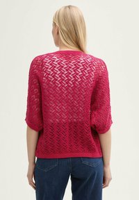 Pull en tricot rose vif avec un motif texturé et ajouré, des manches courtes et un ourlet côtelé. Présente une coupe ample et un design décontracté.