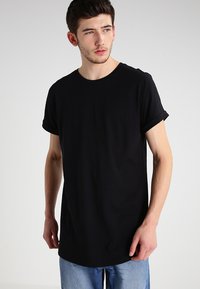 Camiseta de algodón negra con cuello redondo, mangas cortas remangadas y un corte relajado. La tela es suave con un ligero estiramiento, sin adornos visibles.