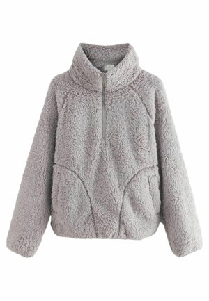 Gros plan d'une veste en tissu gris, duveteux et texturé, avec une fermeture éclair argentée visible, montrant un matériau doux et épais.
