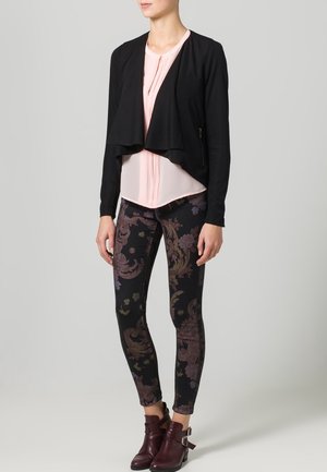Cardigan corto nero, blusa plissettata rosa, leggings a fantasia con design floreale in colori scuri e stivali alla caviglia bordeaux con fibbie.