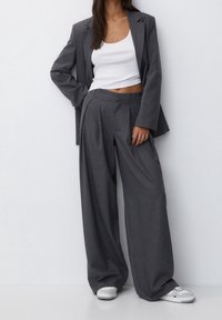 Grijze pinstripe blazer met bijpassende wijde broek, gecombineerd met een witte fitted tanktop. De outfit heeft een op maat gemaakt ontwerp en een ontspannen pasvorm.