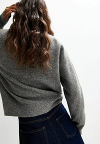 Grijze wollen sweater met een relaxte pasvorm en verlaagde schouders, gecombineerd met een donkere denim rok met contrasterende stiksels en zakken.