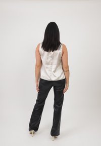 Top bianco in satin senza maniche con schiena bassa, abbinato a pantaloni a gamba larga in ecopelle nera. L'outfit presenta una texture pulita e liscia.