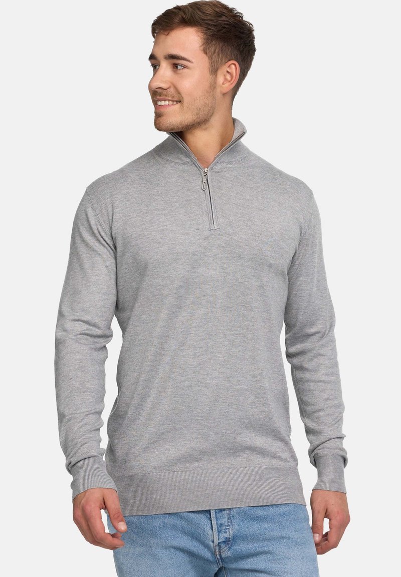 Pull-over gris à manches longues avec fermeture éclair quart de longueur, poignets et ourlet côtelés. Confectionné dans un tissu doux à texture lisse, porté avec un jean bleu clair.