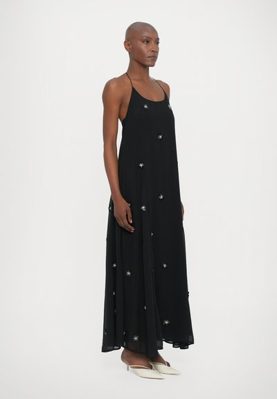 Black, flowy, sleeveless dress with delicate silver embellishments. Features a loose fit and an elongated skirt. Smooth fabric texture.