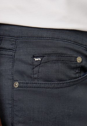 Donkerdenim broek heeft een klein vakje met zilveren hardware en een decoratief hondenmotief. Textuurstof met een subtiel patroon.