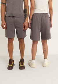 Gray athletic shorts with an elastic waistband, knee-length, paired with varying sneaker styles. One person shows a tattoo on the leg.