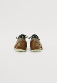 Sneakers in brown and green with a textured fabric upper, cushioned back, and a light-colored rubber sole featuring grip patterns.