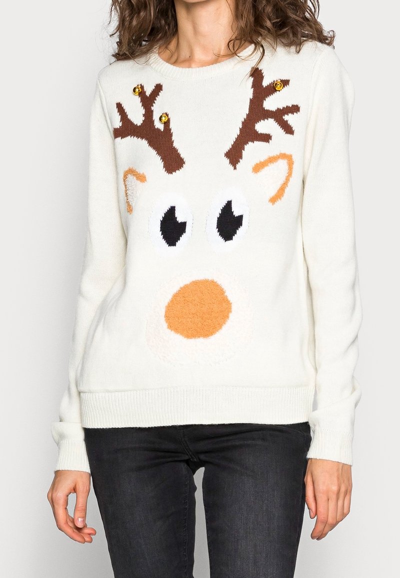 Pull blanc avec un motif visage de renne comprenant des bois marron avec des grelots dorés, de grands yeux et un nez orange porté par une personne.