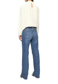 Blouse crème avec un col haut et un détail en forme de goutte d'eau ; associée à un jean bleu clair ample avec des poches arrière.