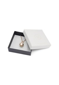 Guldtonad hängande halsband med cirkulär design, prydd med texturerade prickar, visad i en svart och vit låda med mjuk inredning.