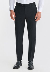 Czarne spodnie materiałowe wykonane z gładkiego materiału, z prostymi nogawkami, plisami oraz paskiem z zapięciem na guzik.