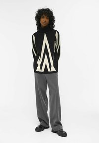 Maglione nero e crema con un motivo a zigzag, design a collo alto, abbinato a pantaloni larghi grigi e scarpe chunky nere.