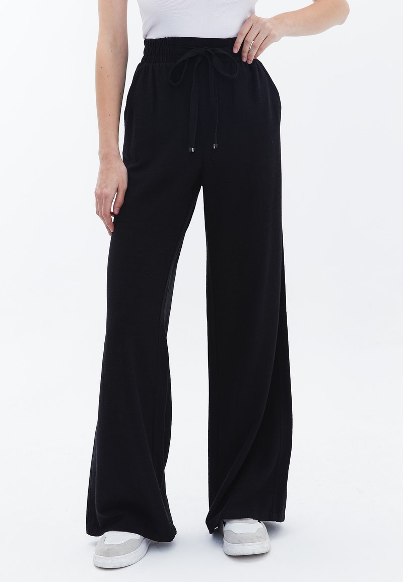 Pantaloni neri a gamba larga realizzati in tessuto morbido con vita regolabile e elastico, dotati di tasche laterali e una vestibilità rilassata.
