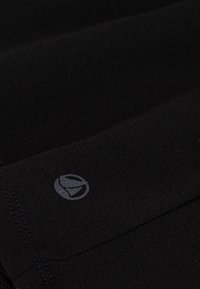 Schwarzes Stoffhemd mit strukturiertem Finish und einem kleinen, grauen Logo, das im unteren Bereich aufgedruckt ist. Einfaches, geradliniges Design.