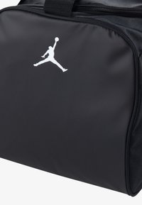 Sort nylon duffel bag med en glat overflade, prydet med et fremtrædende hvidt Jumpman-logo. Udstyret med lynlås og top-håndtag.