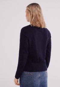 Marineblauw gebreide trui met een geribde zoom en manchetten, met een klassieke ronde halslijn en een relaxed fit. Zachte textuur met minimale details.
