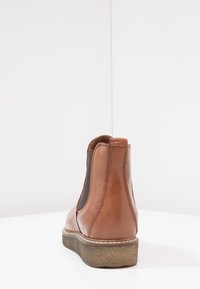 Brown leather ankle boot with elastic side panels, round toe, and textured rubber sole. Contrasting stitching and back pull tab detail.