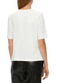 T-shirt blanc à manches courtes en tissu doux, avec un col rond et une coupe droite, associé à un pantalon en cuir noir.