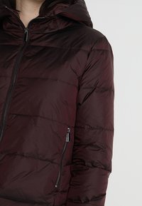 Doudoune bordeaux avec capuche, dotée d'une fermeture zippée, d'une poche latérale zippée et d'un motif matelassé pour l'isolation et la chaleur.