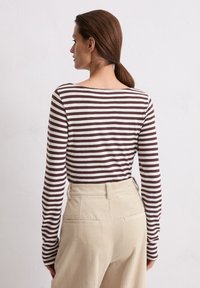 Brązowa i kremowa w paski koszula z długim rękawem, wykonana z gładkiego materiału, z okrągłym dekoltem i luźnym krojem, zestawiona z wysokim stanem spodni z kordurowej tkaniny.