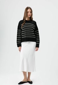 Pull rayé noir et blanc à coupe ample, associé à une jupe midi blanche. Des ballerines noires complètent la tenue. Design simple et minimaliste.