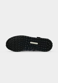 Μαύρη σόλα παπουτσιού Adidas με στρογγυλές αντιολισθητικές εξογκώσεις και λογότυπο Adidas στο κέντρο πάνω σε απλό ανοιχτό γκρι φόντο.
