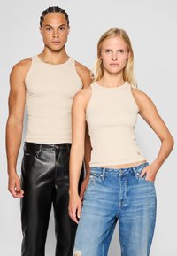 Dva modela nosita bež rebraste majice bez rukava. Jedan model kombinuje sa crnim kožnim pantalonama, dok drugi nosi svijetloplave poderane traperice.