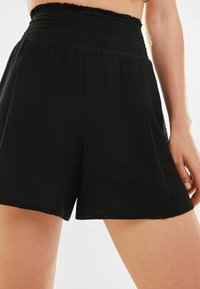 Svarta shorts med smockad midja, tillverkade av mjukt tyg. Designen har löst sittande ben och en minimalistisk stil.